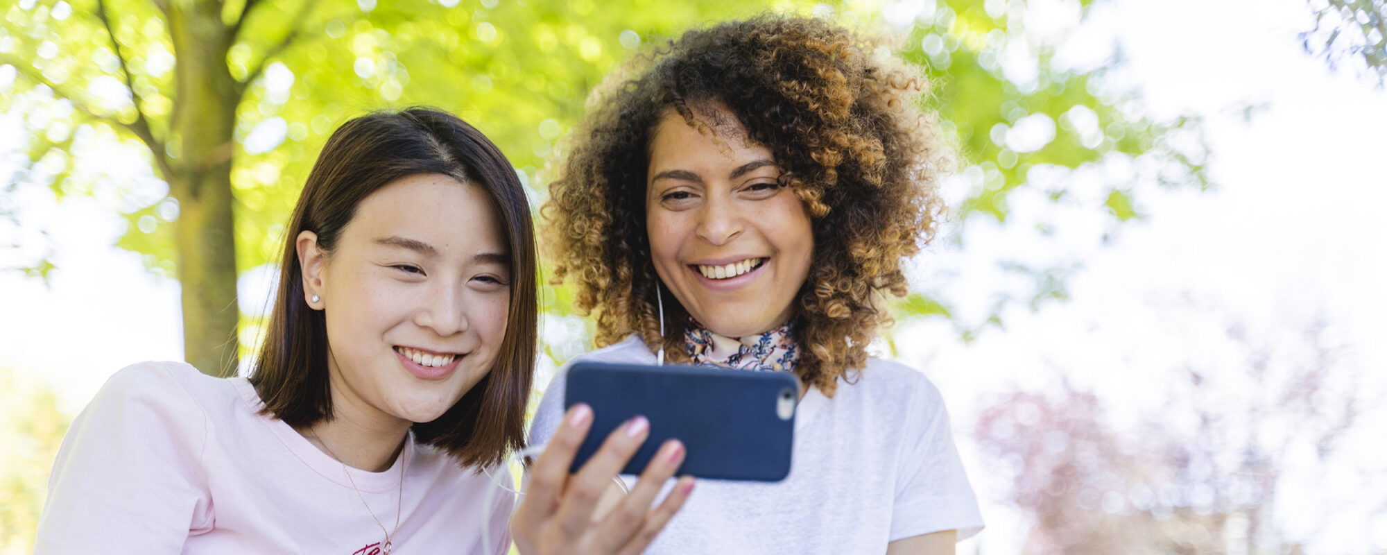 Two happy women with cell phone and earphones in park