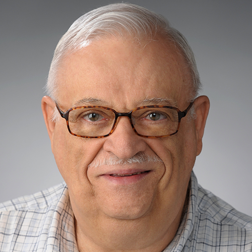 Fred Carriere. Man with white hair looks at camera. He has a white mustache and tortoise shell glasses and a white plaid shirt. 