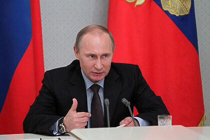 Russian President Vladimir Putin speaks from behind a desk with flags behind him.